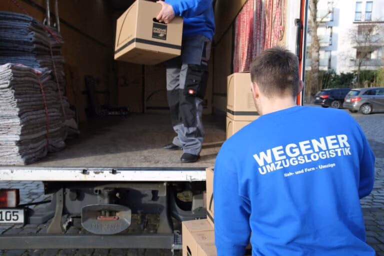 Zwei Umzugshelfer des Umzugsunternehmens Wegener Umzugslogistik in Köln beladen einen Umzugstransporter.