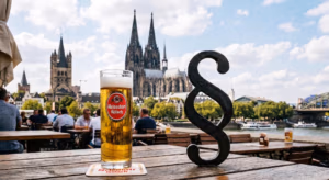 Ein Bild einer Außengastronomie vor der Kölner Skyline an einem sonnigen Tag. Auf dem Tisch steht ein Kölschglas.